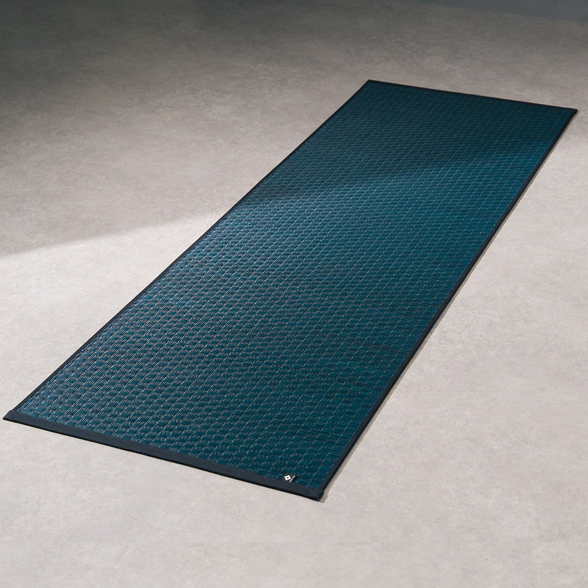 A navy Jimon igusa tatami yoga mat unrolled on a wood floor.