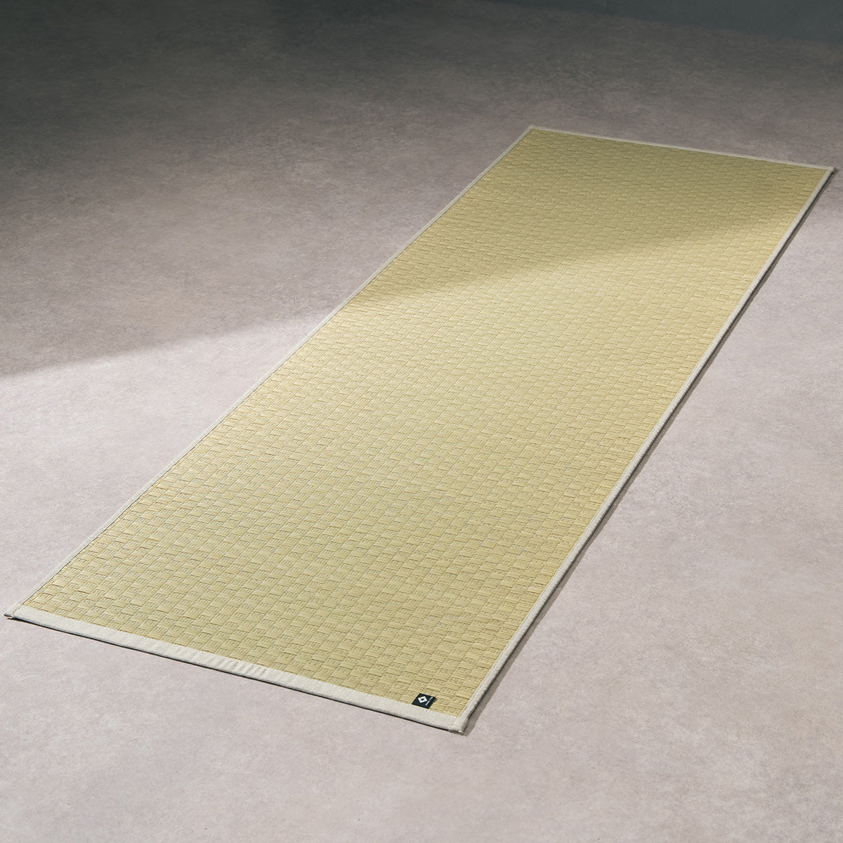 A natural undyed igusa tatami yoga mat unrolled on a wood floor.