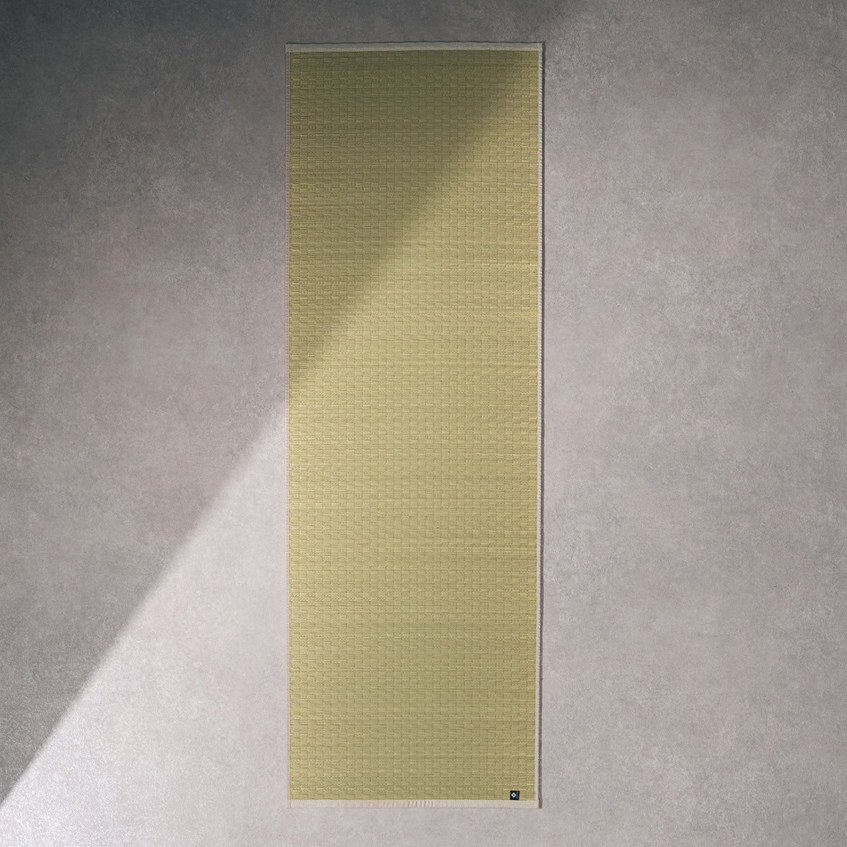 A natural undyed igusa tatami yoga mat unrolled on a wood floor.