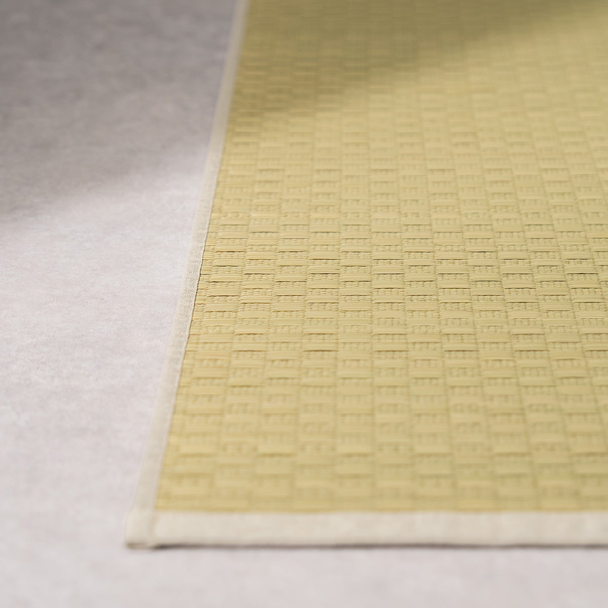 A natural undyed igusa tatami yoga mat unrolled on a wood floor.