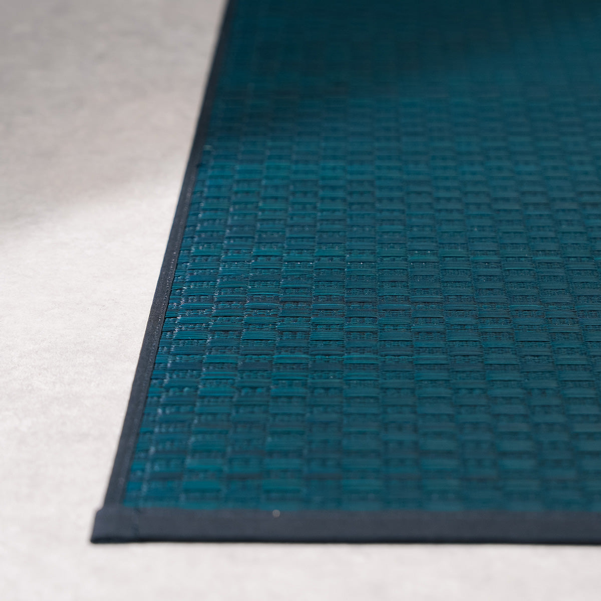 A navy Jimon igusa tatami yoga mat unrolled on a wood floor.