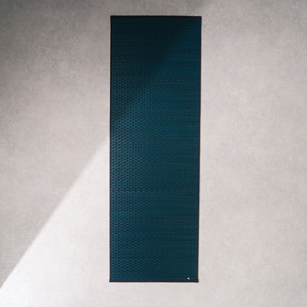 A navy Jimon igusa tatami yoga mat unrolled on a wood floor.