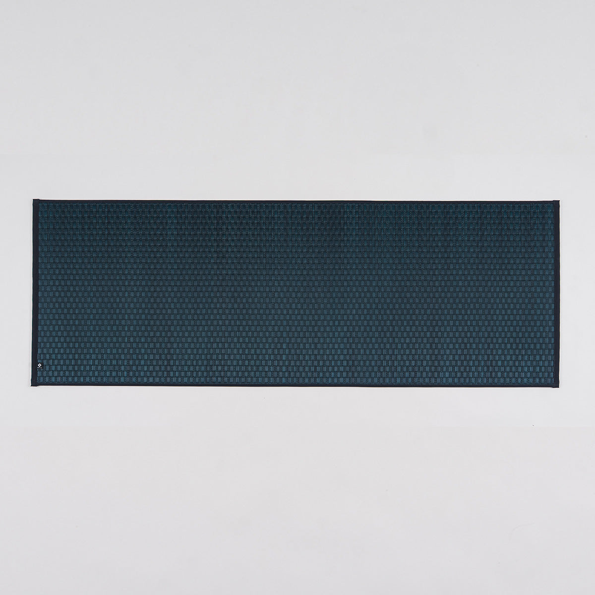 A navy Jimon igusa tatami yoga mat unrolled on a wood floor.