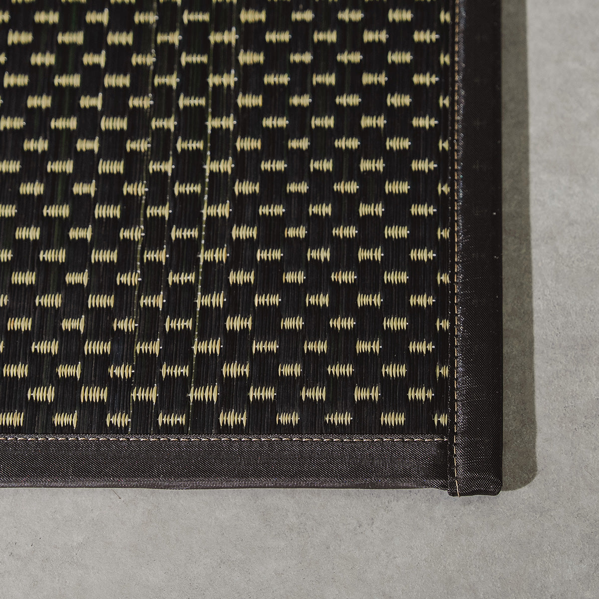 A folded three-fold black igusa tatami mat on a wood floor.